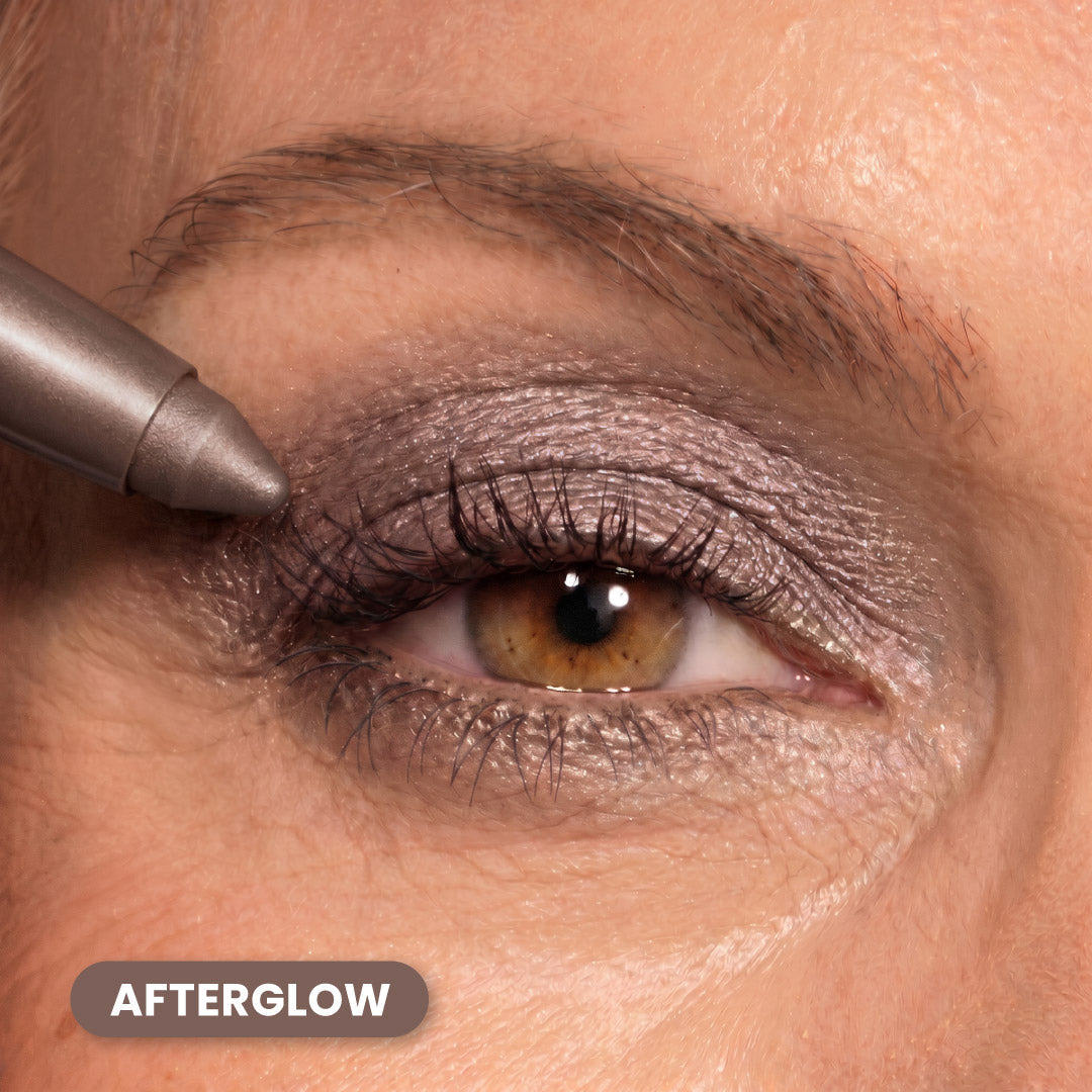 A close-up of a persons eye with metallic purple eyeshadow being applied using a makeup pencil. The text AFTERGLOW appears in the bottom left corner.