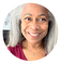 A woman with long gray hair smiles at the camera. She is wearing a maroon top and is pictured in close-up with a light-colored background.
